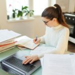 A woman with glasses on her job, utilizing her laptop and managing documents efficiently in a home