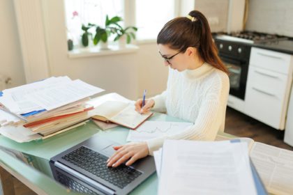 A woman with glasses on her job, utilizing her laptop and managing documents efficiently in a home