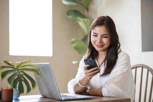 Attractive and happy young Asian girl reading a book and use laptop at a table in her minimal living