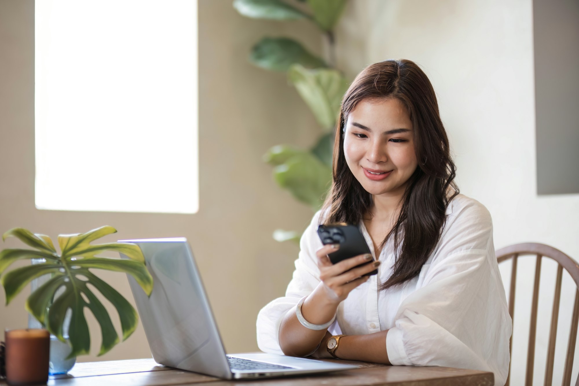 Attractive and happy young Asian girl reading a book and use laptop at a table in her minimal living