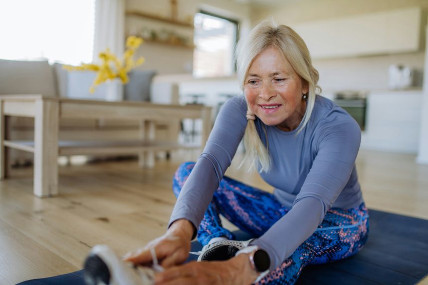 Fit senior woman doing stretching exercise at home, active lifestyle concept.