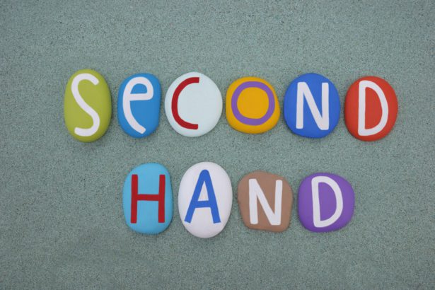 Second hand, creative logo composed with multi colored stone letters over green sand